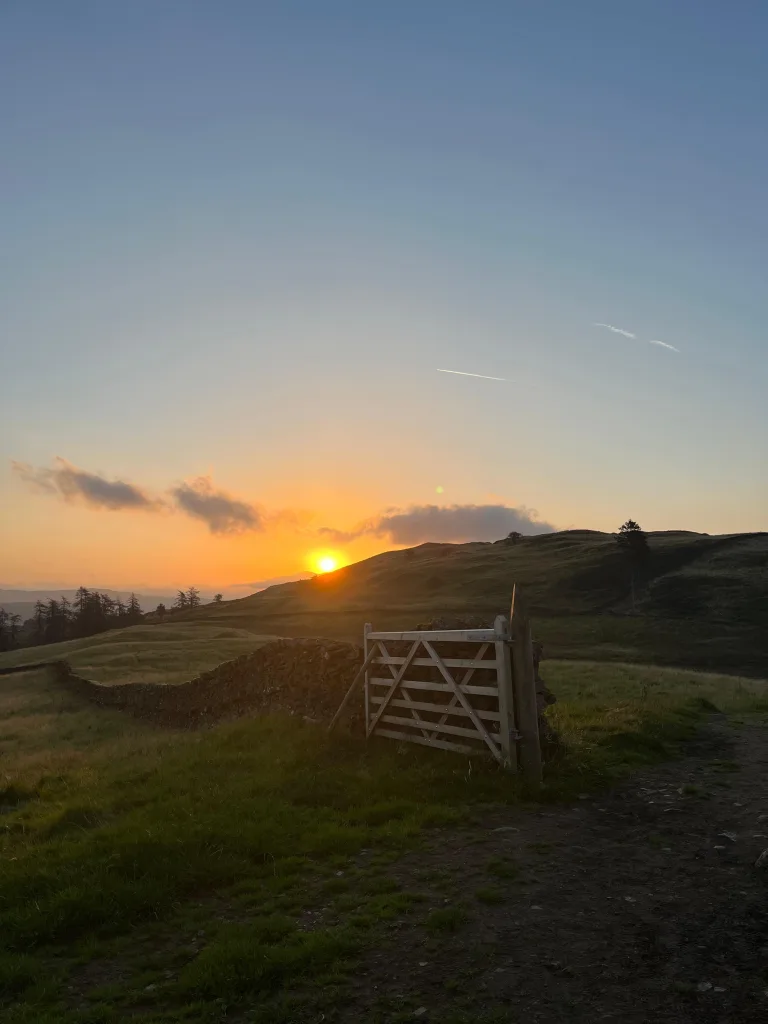 Things to do in Windermere: a field with an open gate at sunset above the village